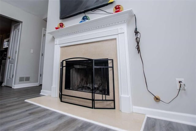 room details with visible vents, a fireplace, baseboards, and wood finished floors