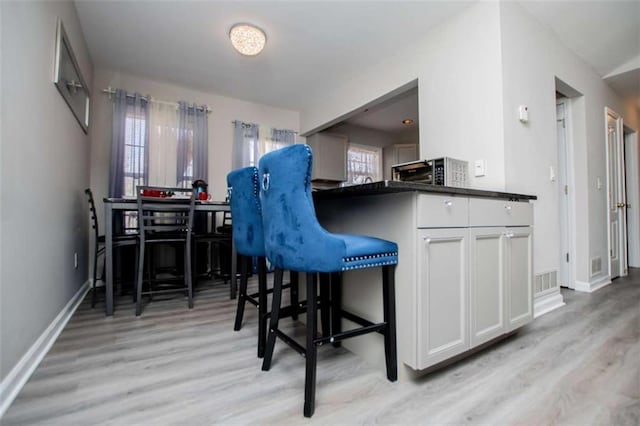 kitchen with white cabinetry, visible vents, baseboards, light wood-type flooring, and dark countertops