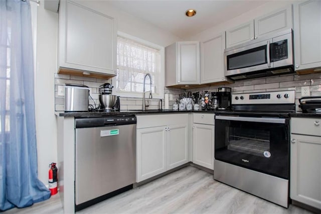 kitchen featuring dark countertops, light wood-style flooring, backsplash, appliances with stainless steel finishes, and a sink