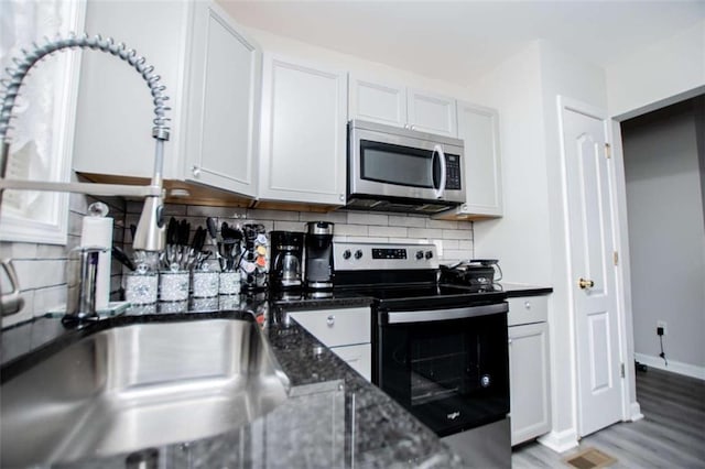 kitchen with tasteful backsplash, appliances with stainless steel finishes, white cabinetry, dark stone counters, and light wood-type flooring