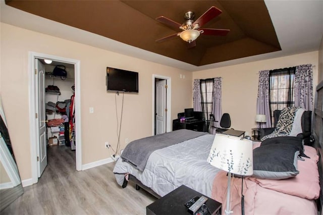 bedroom featuring a raised ceiling, a closet, a spacious closet, light wood-style floors, and baseboards