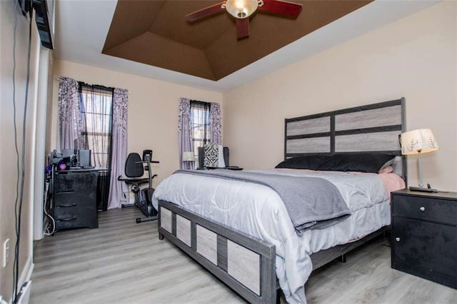 bedroom with light wood-style floors, a tray ceiling, and a ceiling fan