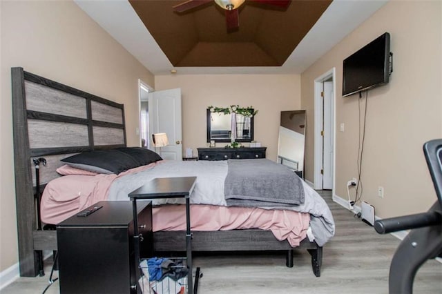 bedroom with a ceiling fan, a tray ceiling, baseboards, and wood finished floors