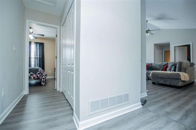 hall featuring lofted ceiling, wood finished floors, visible vents, and baseboards