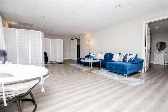 living area with a paneled ceiling, a barn door, wood finished floors, and recessed lighting