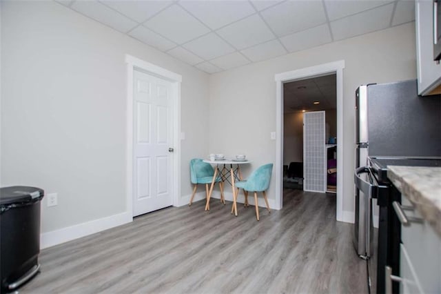 dining room featuring light wood finished floors, baseboards, and a drop ceiling