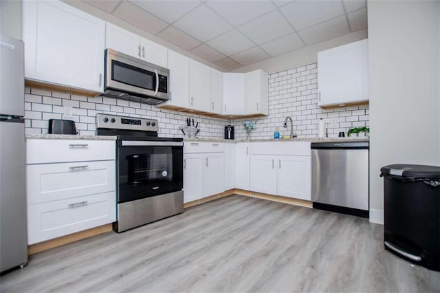 kitchen featuring appliances with stainless steel finishes, decorative backsplash, light wood-style flooring, and white cabinets