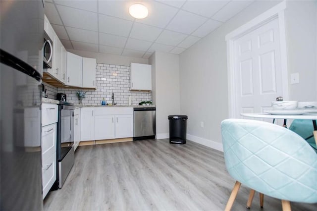 kitchen with appliances with stainless steel finishes, light wood-style floors, white cabinets, and decorative backsplash