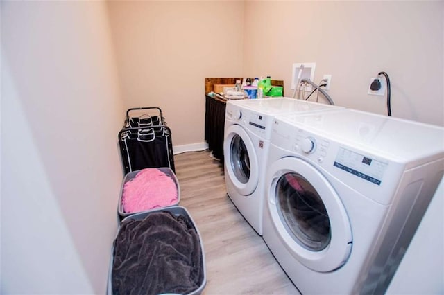 clothes washing area featuring laundry area, baseboards, washer and clothes dryer, and light wood finished floors