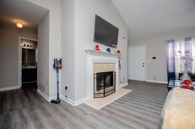 living room featuring vaulted ceiling, a fireplace, wood finished floors, and visible vents