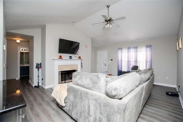 living area featuring lofted ceiling, a fireplace, wood finished floors, a ceiling fan, and baseboards