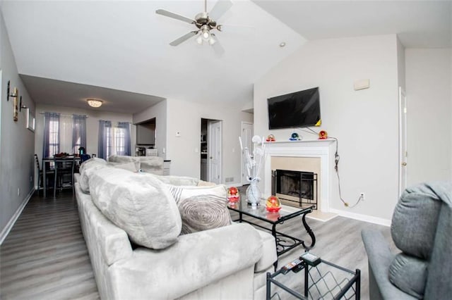 living area with lofted ceiling, baseboards, a fireplace with raised hearth, and wood finished floors