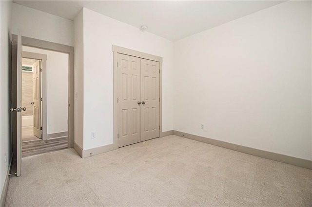 unfurnished bedroom with baseboards, a closet, and light colored carpet