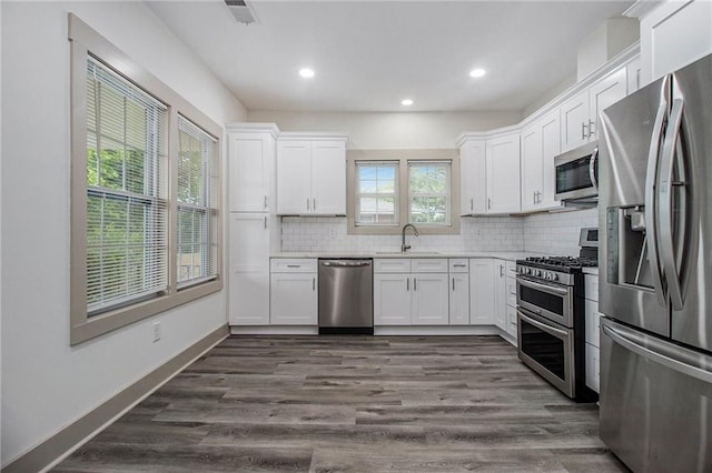 kitchen with stainless steel appliances, a sink, white cabinets, backsplash, and dark wood-style floors