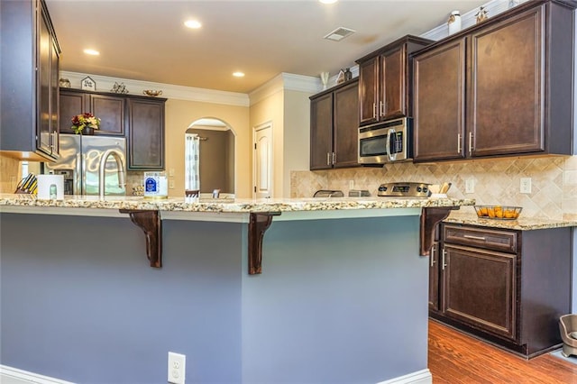 139 Village Park Dr, Newnan, GA 30265 - kitchen featuring appliances with stainless steel finishes, arched walkways, crown molding, a kitchen bar, and light stone countertops