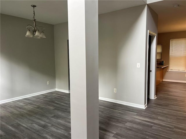 empty room with dark wood-type flooring and a notable chandelier