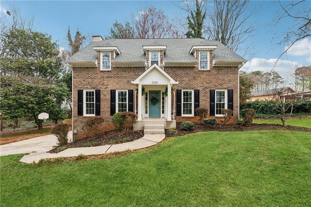 view of front of home with brick siding, a chimney, a front yard, and roof with shingles