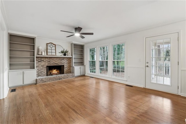 unfurnished living room with visible vents, plenty of natural light, built in shelves, and ceiling fan