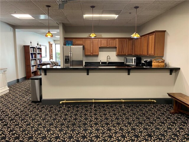 kitchen with stainless steel appliances, sink, a paneled ceiling, carpet floors, and pendant lighting