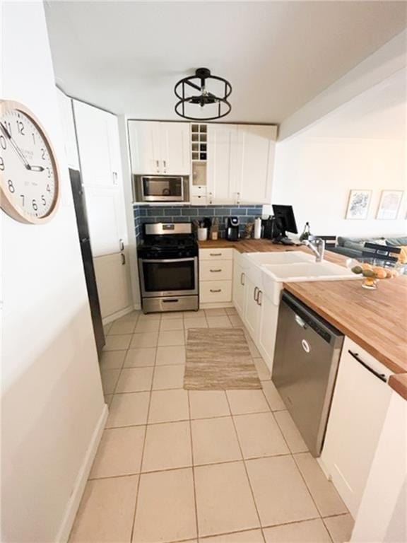 kitchen with stainless steel appliances, butcher block counters, white cabinets, and glass insert cabinets