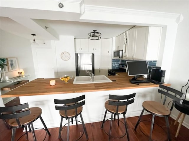 kitchen featuring stainless steel appliances, a sink, wood counters, a peninsula, and a kitchen bar