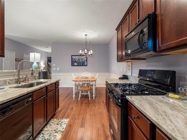 kitchen featuring black appliances, sink, light hardwood / wood-style floors, pendant lighting, and a chandelier