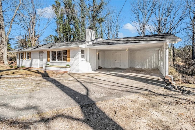 back of house featuring driveway, a chimney, an attached carport, and brick siding