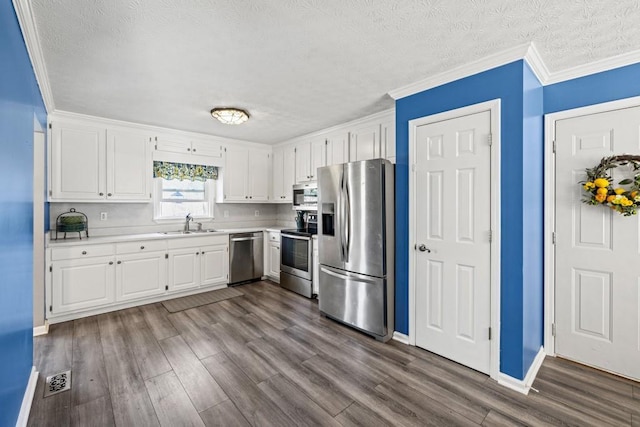 kitchen featuring hardwood / wood-style floors, crown molding, sink, appliances with stainless steel finishes, and white cabinetry