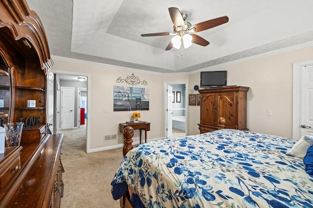 carpeted bedroom with connected bathroom, a tray ceiling, ceiling fan, and ornamental molding