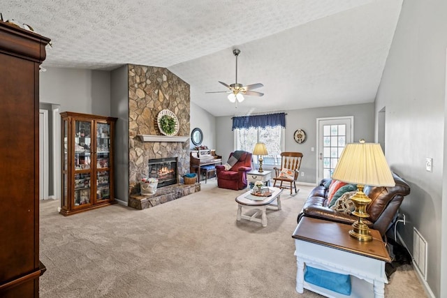 living room with ceiling fan, a stone fireplace, lofted ceiling, a textured ceiling, and light carpet