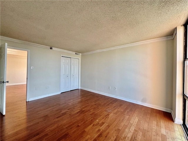 unfurnished room featuring a textured ceiling, crown molding, baseboards, and wood-type flooring