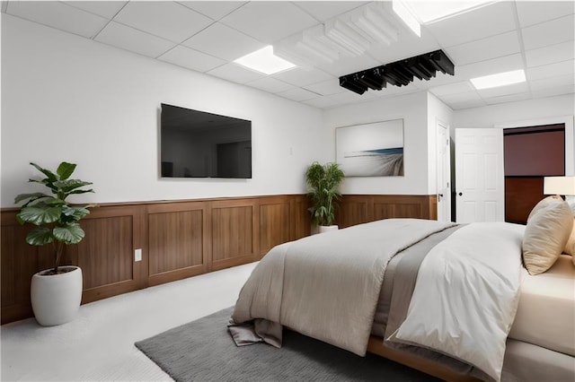 bedroom featuring a paneled ceiling, light colored carpet, and wainscoting