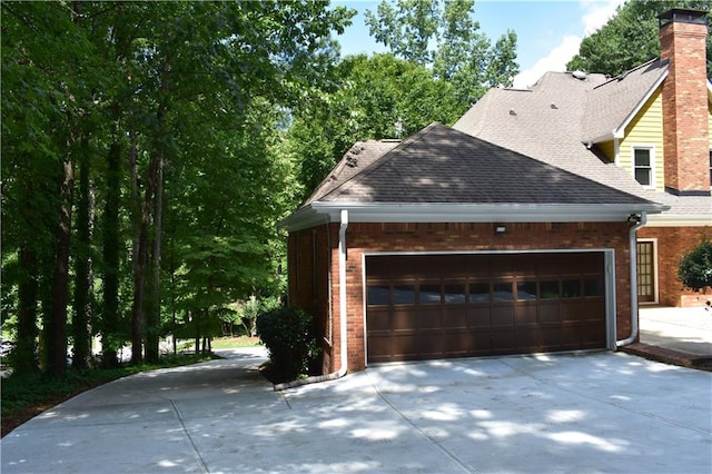 view of side of home featuring an attached garage, brick siding, roof with shingles, and driveway