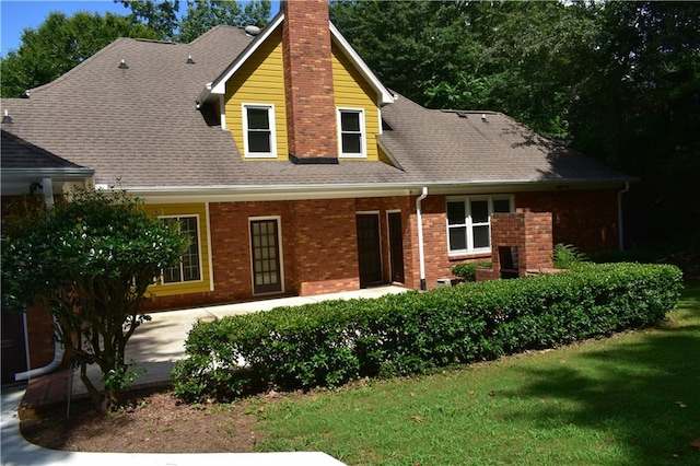 view of front facade featuring a front yard, brick siding, roof with shingles, and a chimney