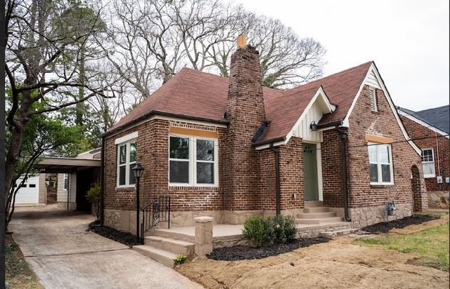 tudor house with a carport, brick siding, driveway, and a chimney