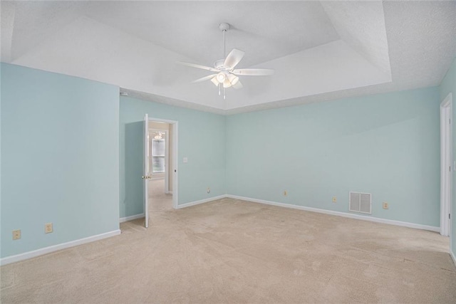 unfurnished room with ceiling fan, light colored carpet, a textured ceiling, and a tray ceiling