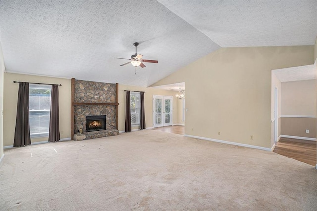 unfurnished living room with ceiling fan with notable chandelier, a stone fireplace, lofted ceiling, and light carpet