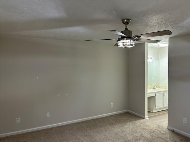 unfurnished room with ceiling fan, sink, light colored carpet, and a textured ceiling