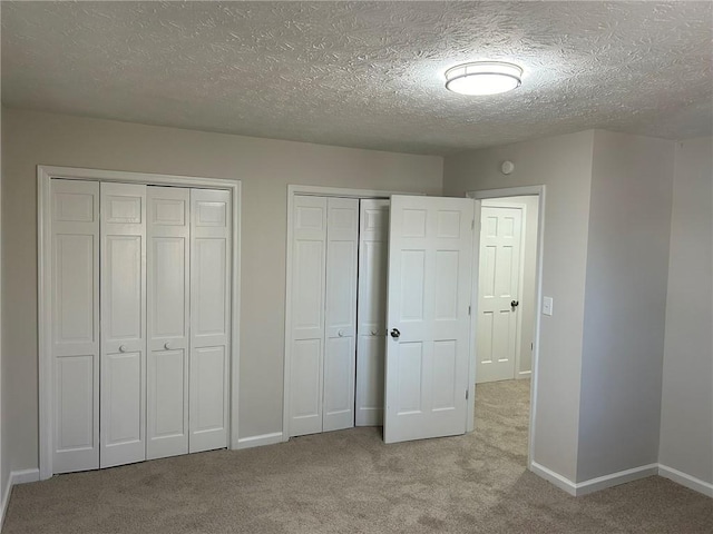 unfurnished bedroom featuring light colored carpet, a textured ceiling, and two closets