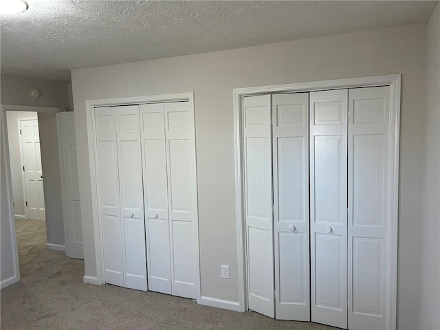 unfurnished bedroom with light colored carpet, a textured ceiling, and two closets