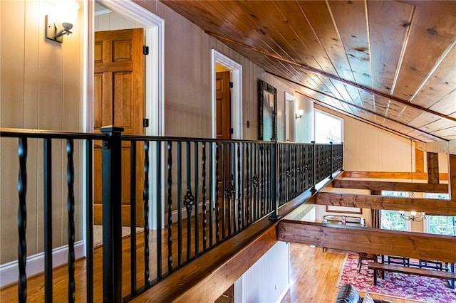 corridor with lofted ceiling, wooden walls, wooden ceiling, and light hardwood / wood-style floors