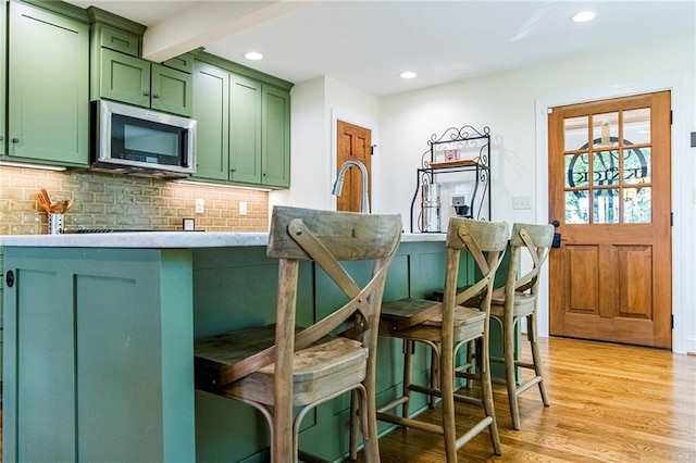 kitchen with backsplash, light hardwood / wood-style floors, a breakfast bar, and green cabinetry