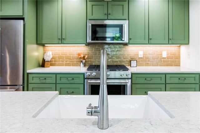 kitchen featuring light stone counters, tasteful backsplash, stainless steel appliances, and green cabinets