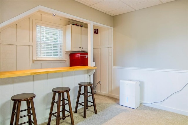 kitchen featuring white cabinets, a paneled ceiling, a breakfast bar area, and light colored carpet