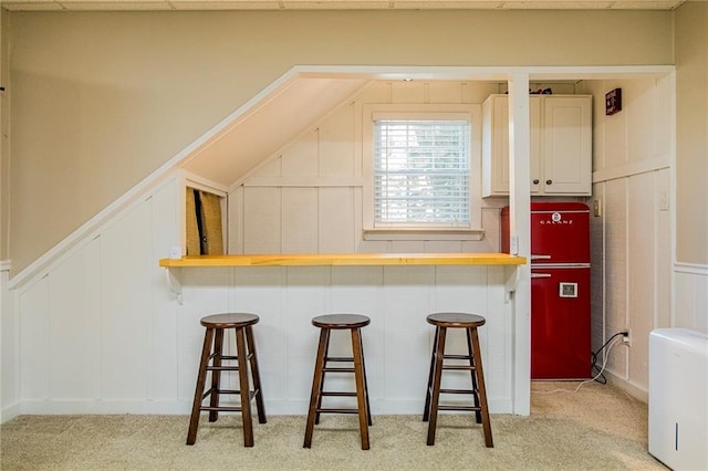 kitchen with a breakfast bar, kitchen peninsula, light carpet, and white cabinets