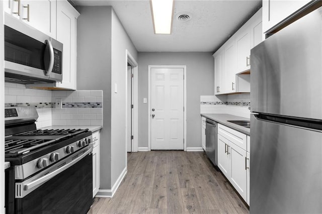 kitchen with white cabinets, wood finished floors, baseboards, and appliances with stainless steel finishes