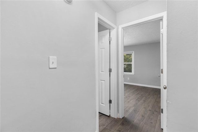 hall featuring dark wood-style floors, a textured ceiling, and baseboards