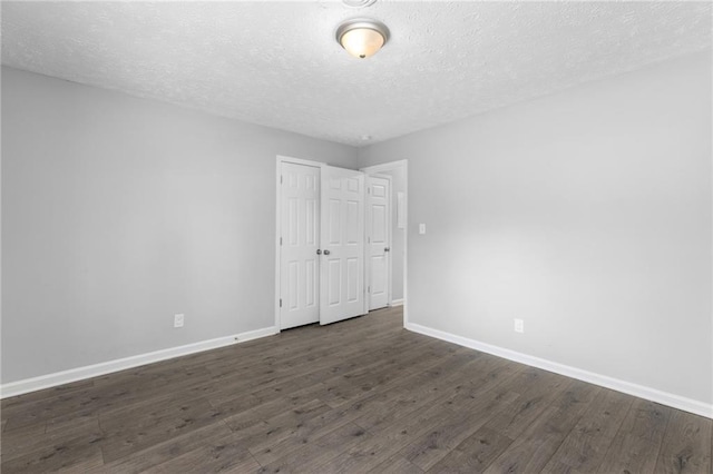 spare room featuring baseboards, a textured ceiling, and dark wood-style floors