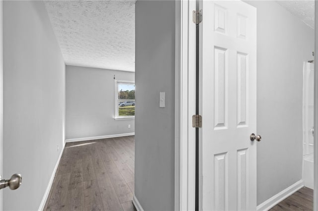 corridor with dark wood-type flooring, baseboards, and a textured ceiling