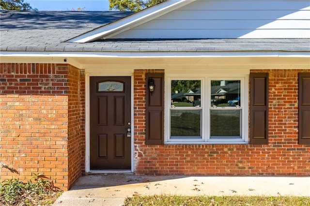 doorway to property featuring brick siding and roof with shingles